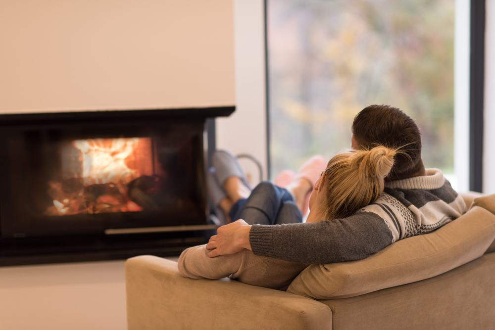 A young couple in winter attire sitting on couch in living room in front of fireplace